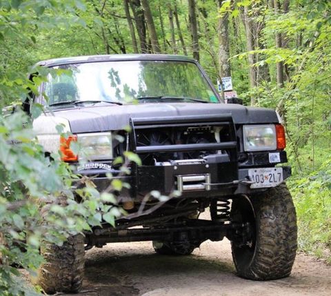 1989 Ford Bronco - A black Ford Bronco navigates a wooded trail, its off-road modifications evident.