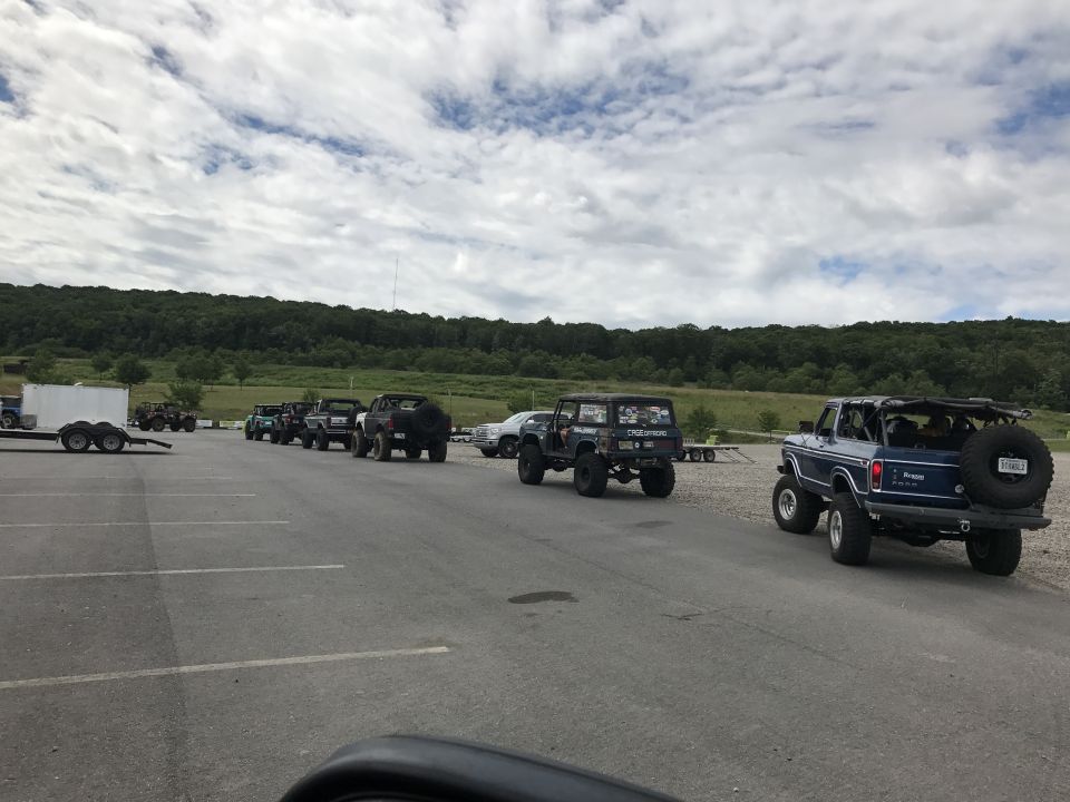 Several off-road SUVs parked in a lot, with a wooded hill in the background