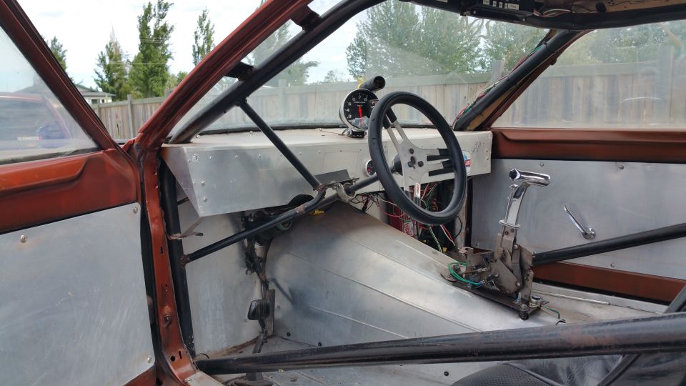 Car interior with roll cage, aftermarket steering wheel, and tachometer