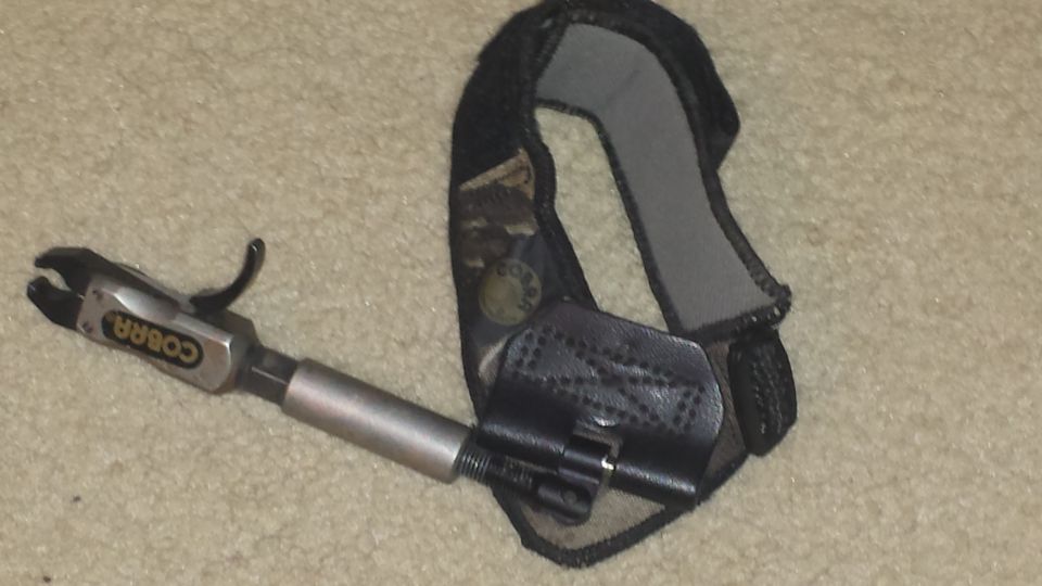 Cobra brand archery release aid with camo wrist strap on beige carpet
