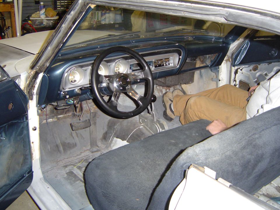 Stripped interior of a white classic coupe with blue dash and black steering wheel in a shop