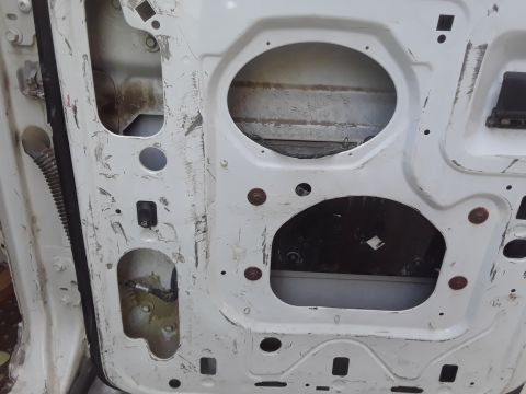1999 Ford E250 - The interior of a white van door shows exposed metal, rust, and wiring, with two large cutouts.