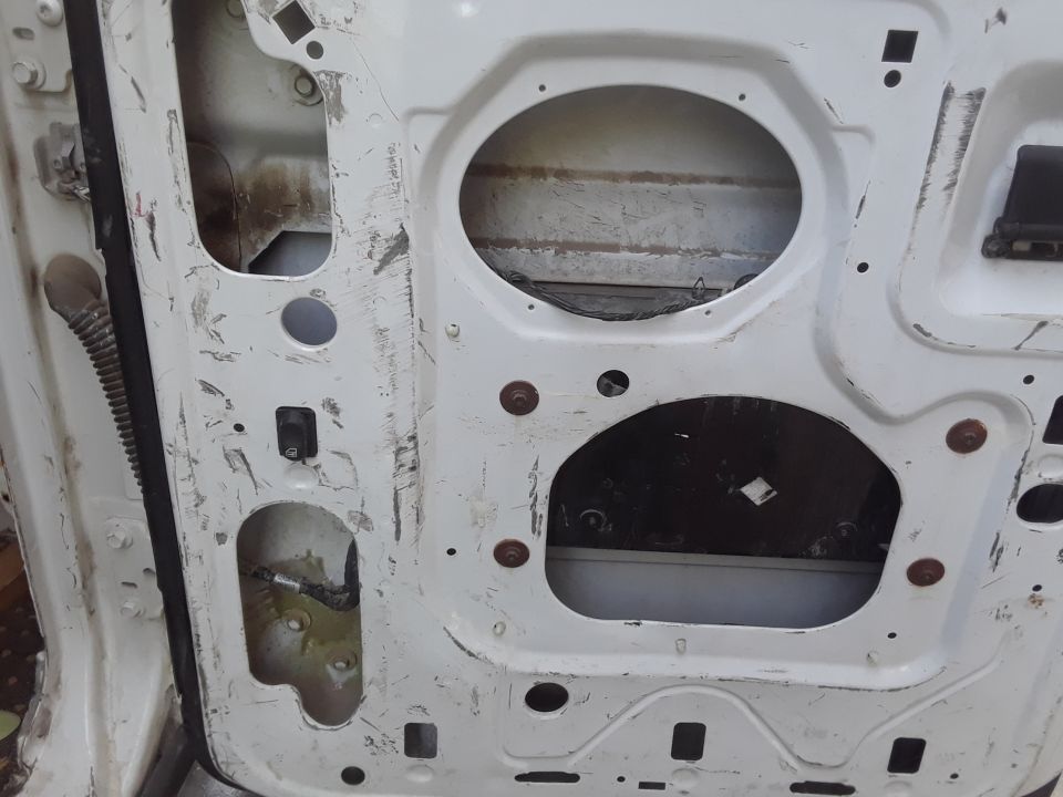 White van door interior with exposed metal, rust, and wiring. Two large oval cutouts are visible
