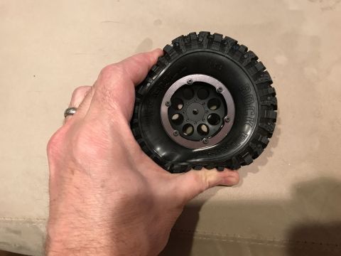 1989 Ford Bronco - A hand squeezes a black RC car tire, revealing its flexible sidewall and detailed tread pattern.