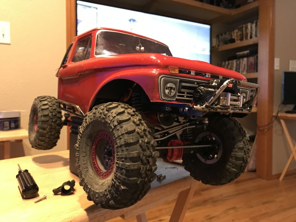 Red RC truck with large tires, winch, and tools on a workbench.