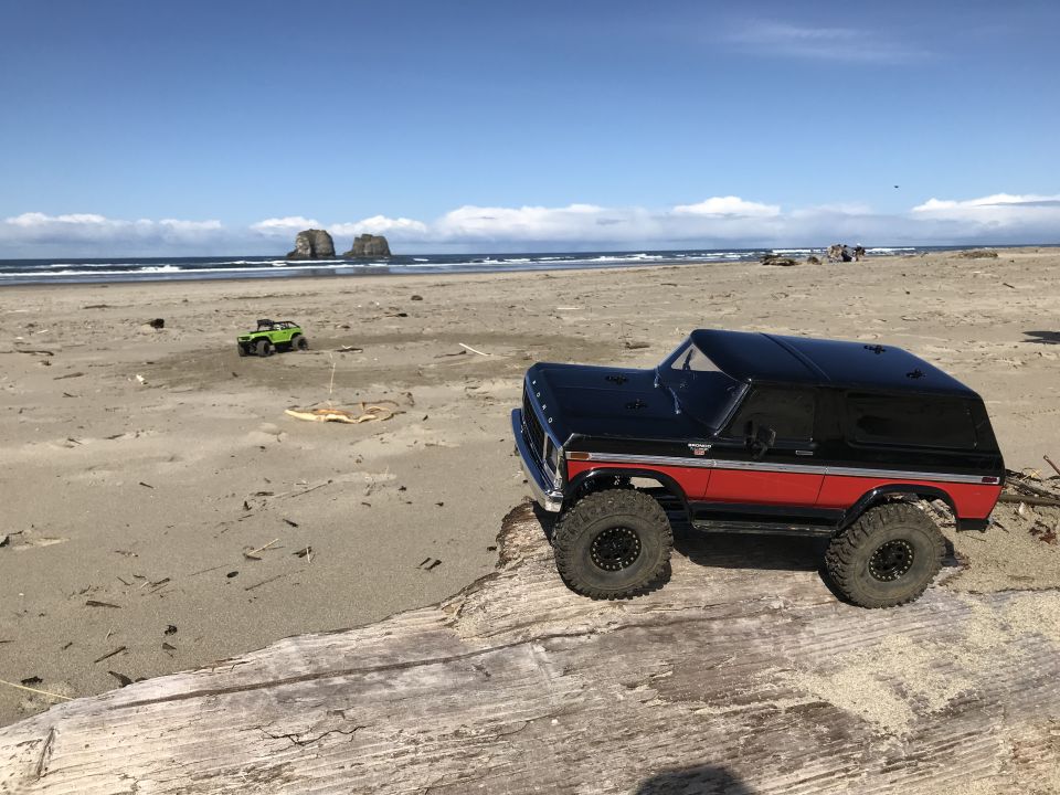 Black and red remote-controlled Ford Bronco on a beach log with ocean in background.