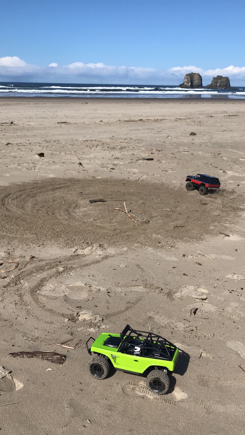 Two remote-controlled off-road vehicles on a sandy beach.