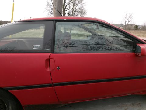Red 1989 Ford Probe coupe, side view, showing driver's door, window, and side mirror.