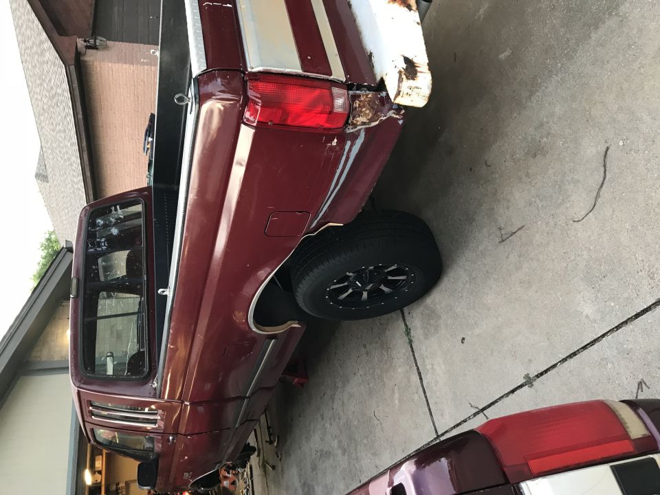 1996 Ford F-150 pickup truck, rear passenger side view, dark red with white stripe, rust damage.