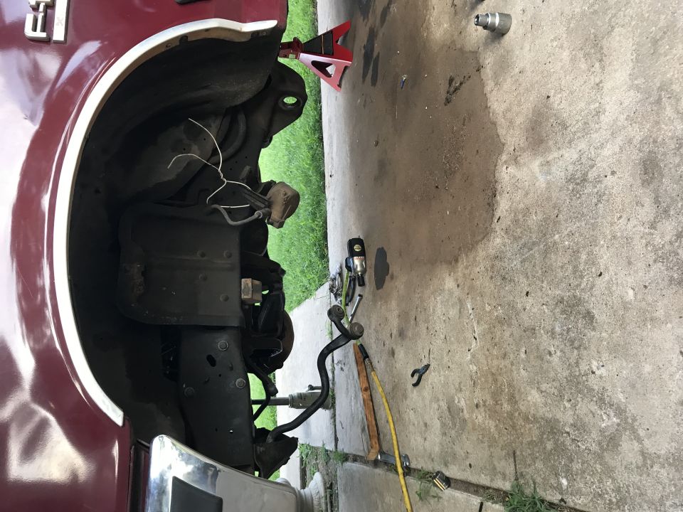 Underside of a red Ford F-150 truck with suspension parts and tools on the ground.