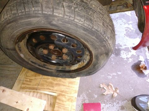 1989 Ford Probe — Flat tire on a black steel wheel with rusty lug nuts, resting on wooden planks.