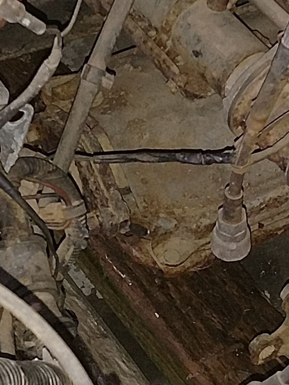 Close-up of rusted vehicle underside with spliced black wire and electrical tape.