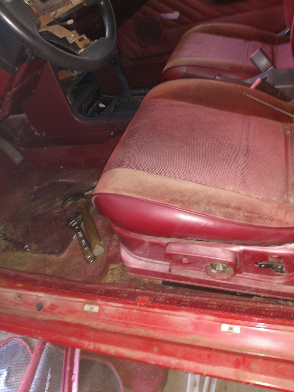 Interior of a red vehicle showing the driver's seat, dashboard, and floor with tools.