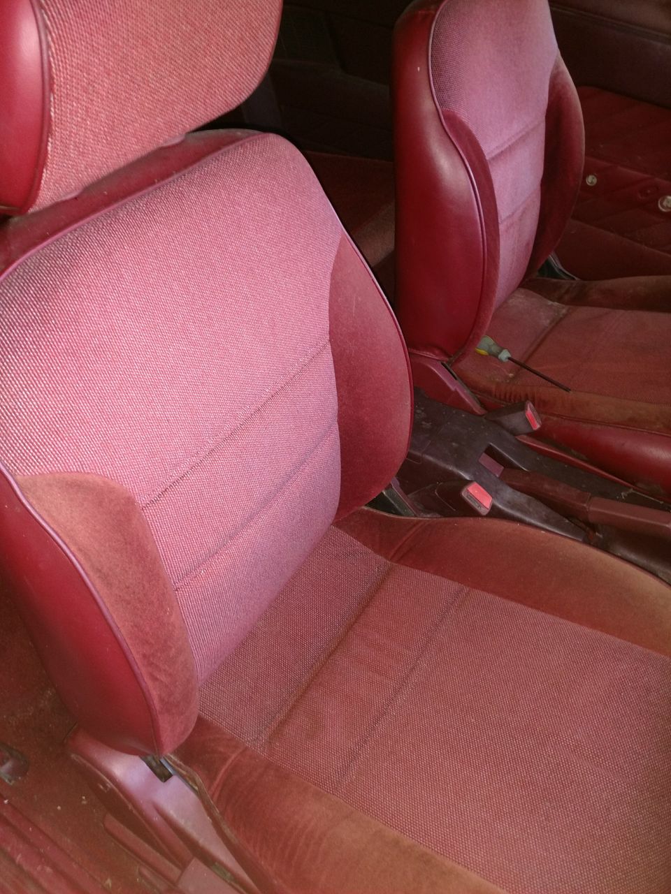 Red fabric and vinyl car seats, driver and passenger side, dusty and worn.