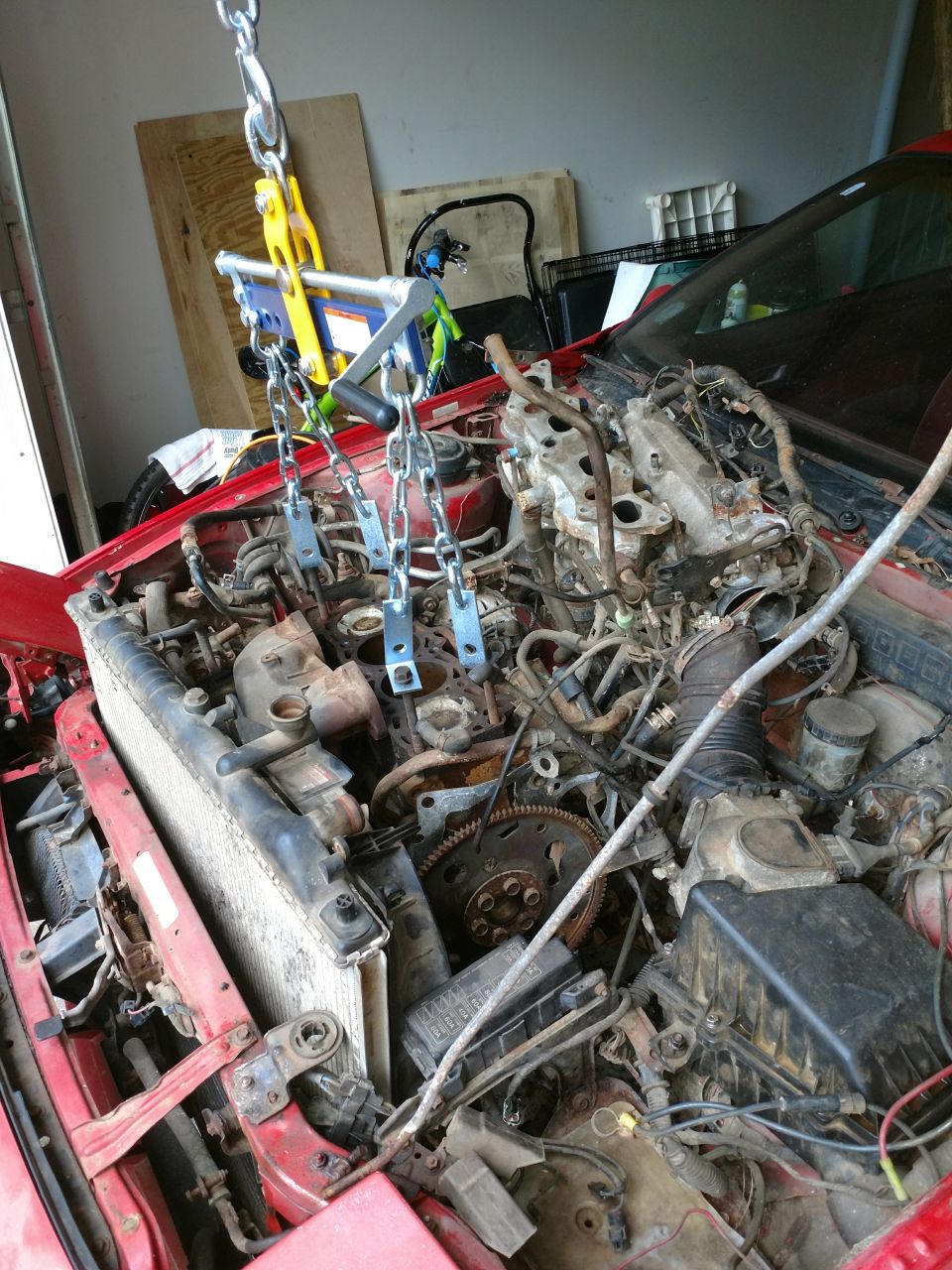 Red car engine bay with engine hoist and chains attached.