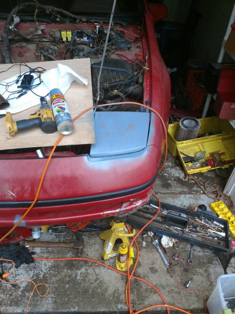 1989 Ford Probe — Disassembled red car front end with tools and parts scattered around.