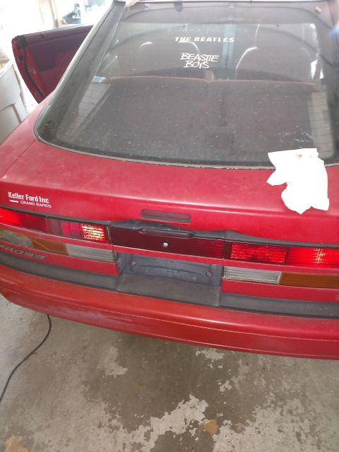 Rear view of a red 1989 Ford Probe with Beatles and Beastie Boys stickers on the window.