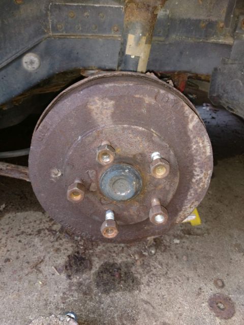1989 Ford Probe - A heavily rusted drum brake assembly is shown attached to the suspension of a vehicle. The brake drum has five lug nuts visible, and the su…