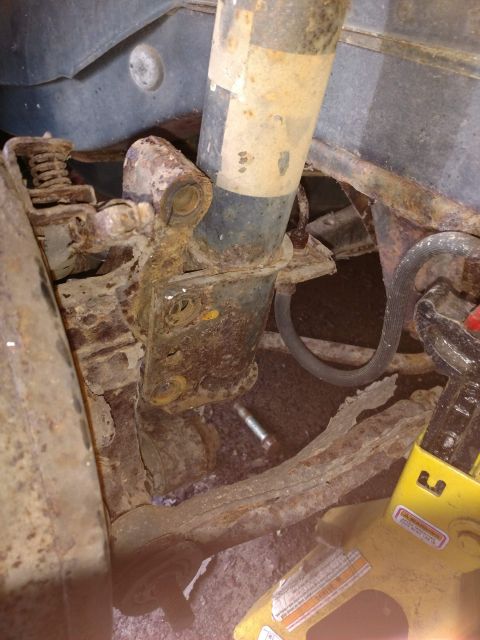 1989 Ford Probe - This image shows heavily rusted suspension components of a vehicle, including a shock absorber and part of a coil spring, with a yellow jac…