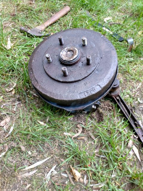 1989 Ford Probe - A rusty brake drum assembly with five wheel studs is resting on grass, with a hammer and other tools visible in the background.