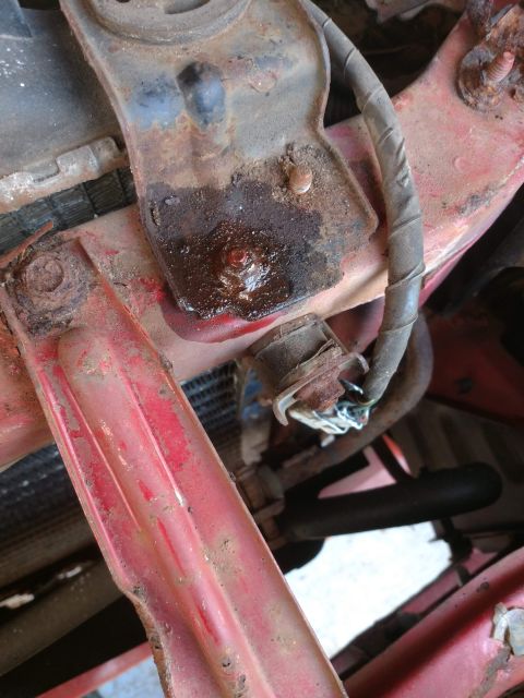 1989 Ford Probe - A close-up view shows a rusted metal bracket with a leaking bolt and a gray electrical wire attached. The bracket is mounted on a red paint…