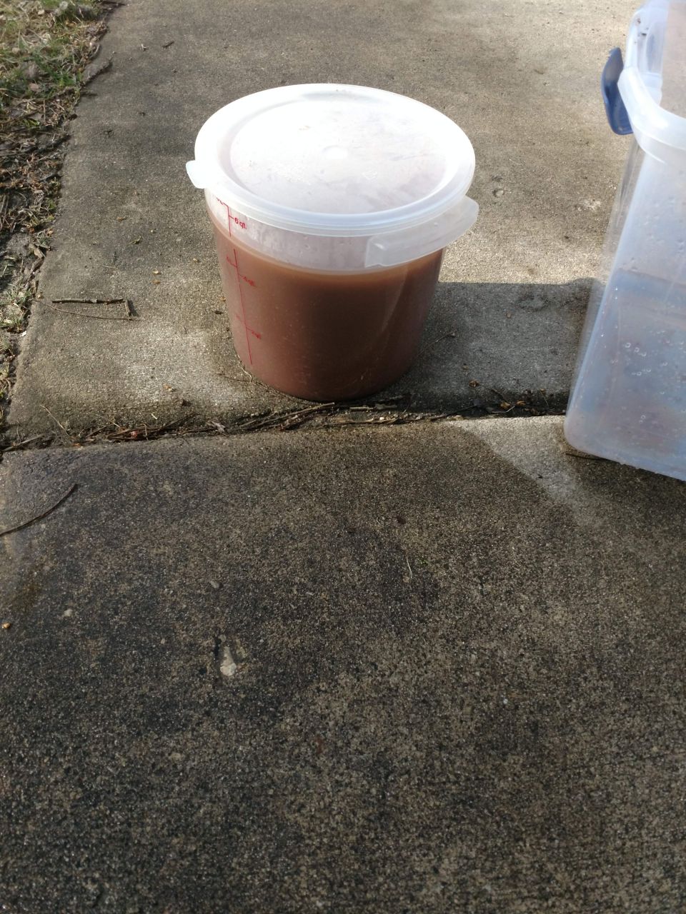 Plastic bucket with brown liquid on concrete