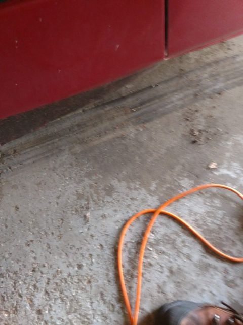 1989 Ford Probe - A close-up view of a red vehicle's lower body panel and a concrete floor with an orange cord and a person's shoe.