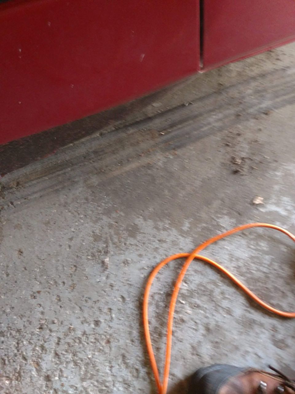 Red vehicle lower panel, concrete floor, orange cord, and a shoe.
