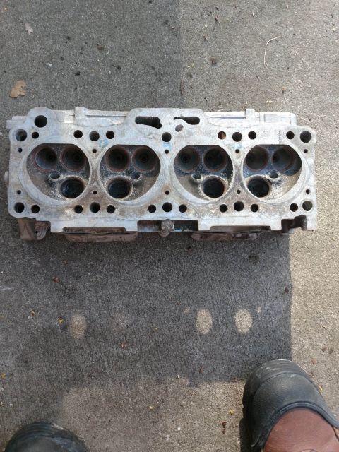 1989 Ford Probe - A top-down view of a four-cylinder engine cylinder head resting on a concrete surface. The cylinder head shows signs of wear and has four d…