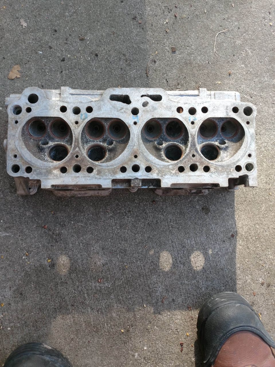 Engine cylinder head with four sets of ports, resting on concrete.