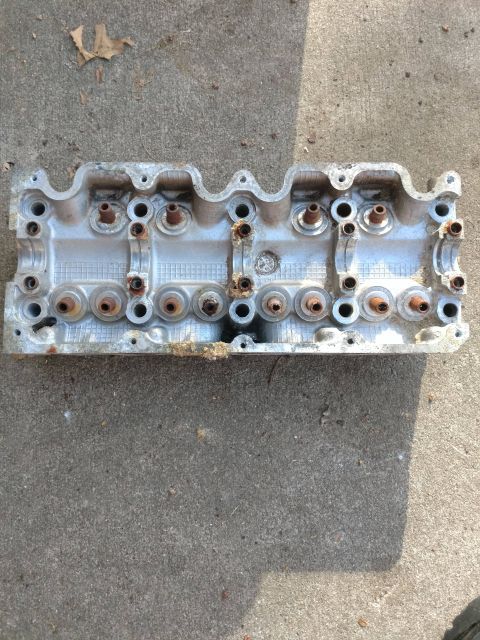 1989 Ford Probe - A top-down view of a used aluminum engine cylinder head with visible rust on the valve stems, lying on a concrete surface.