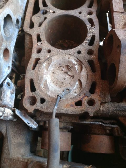 1989 Ford Probe - A close-up view of a heavily rusted engine block, showing cylinder bores and a piston head with a grounding wire attached.