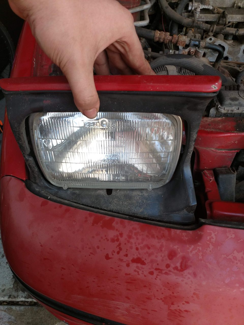 Close-up of a hand holding a red car's headlight assembly.