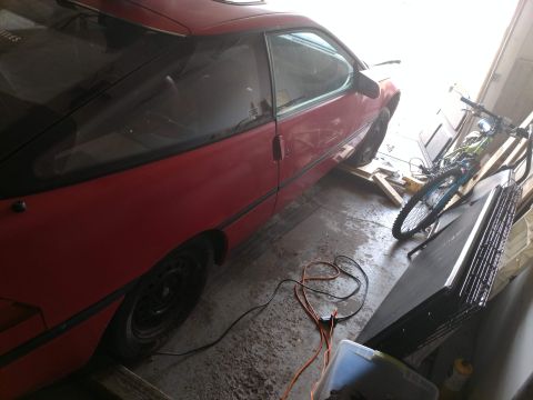 1989 Ford Probe - A red 1989 Ford Probe is parked in a garage next to a bicycle and other stored items. The car is viewed from the rear passenger side, showi…