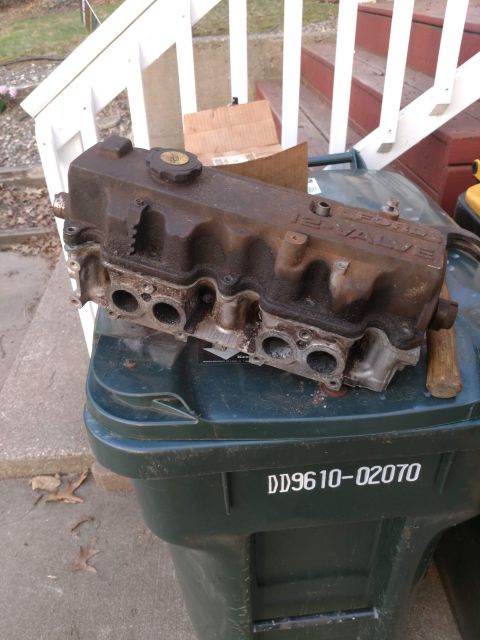 1989 Ford Probe - A rusty Ford 12-valve cylinder head sits on top of a dark green trash can. The cylinder head is positioned at an angle, showing its intake…
