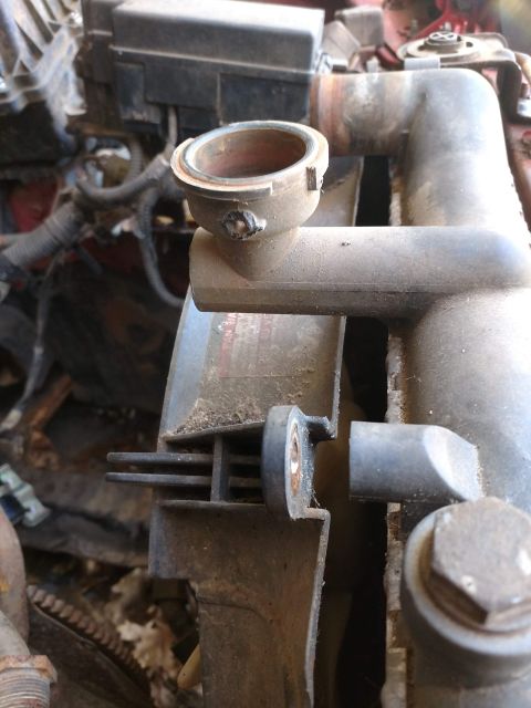 1989 Ford Probe - A close-up view of a radiator cap housing and part of the radiator assembly in a vehicle engine bay. The plastic housing appears worn and d…
