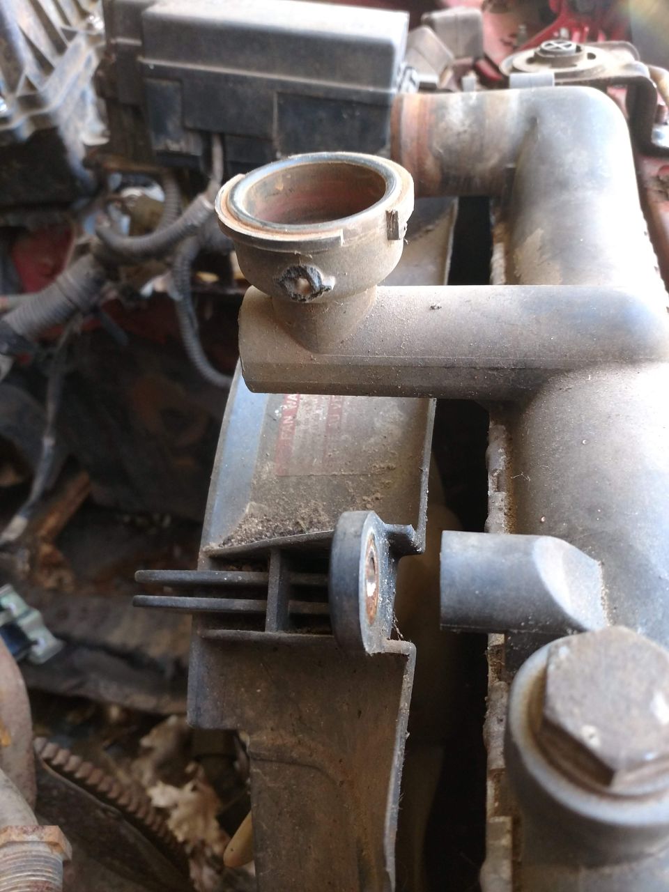 Close-up of a dirty radiator cap housing and part of a car radiator.