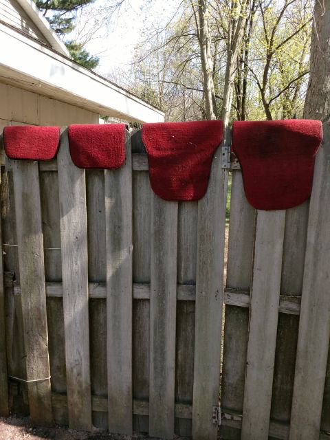 1989 Ford Probe - Four red saddle pads are hanging on a weathered wooden fence. The saddle pads are of varying sizes and shapes.