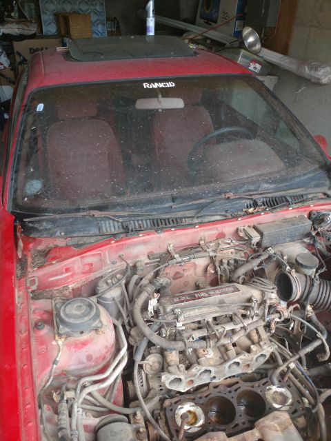 1989 Ford Probe - The engine bay of a red 1989 Ford Probe is shown, with the hood open. The engine is partially disassembled, revealing the cylinders and fue…