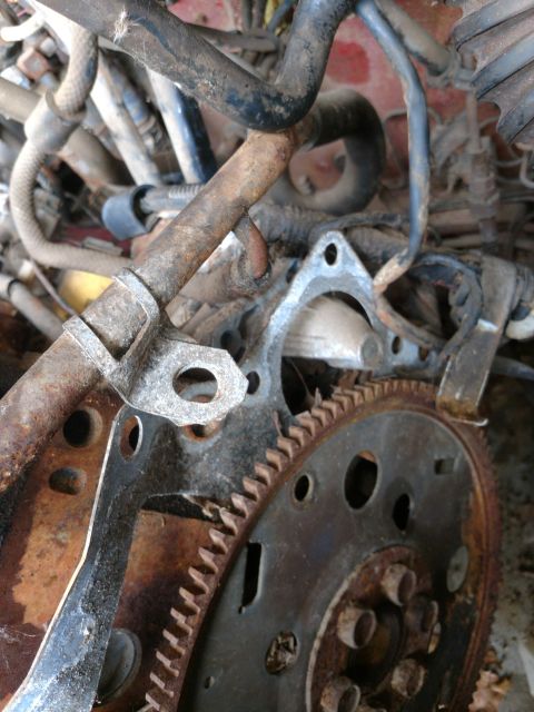 1989 Ford Probe - A close-up view of heavily rusted engine components, including a flywheel with visible teeth and a metal gasket. Various hoses and metal pi…