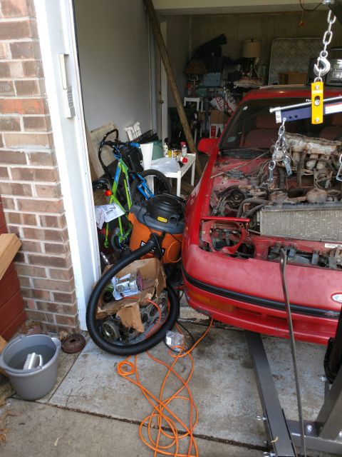 1989 Ford Probe - A red Ford Probe is parked in a garage with its engine removed and supported by an engine hoist. Various tools and car parts are scattered…
