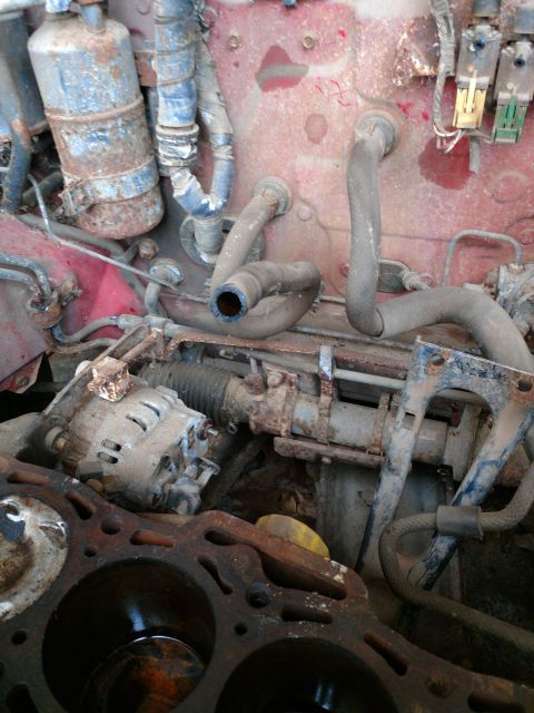 1989 Ford Probe - This is a close-up view of a heavily rusted and dirty engine bay, featuring an alternator, various hoses, and the top of a cylinder head.