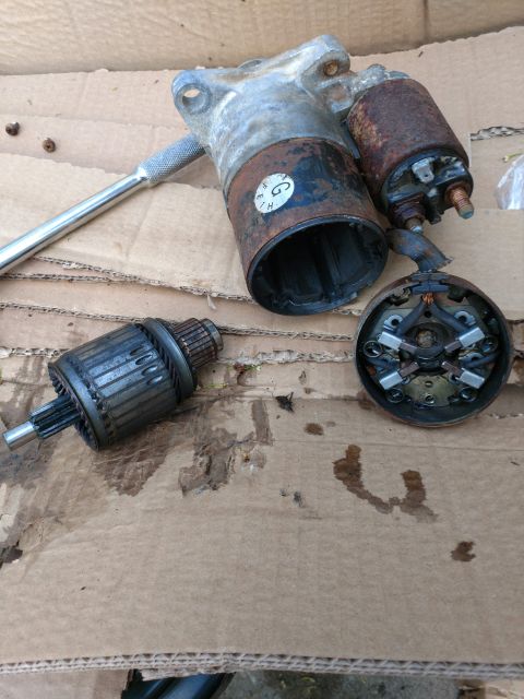 1989 Ford Probe - A disassembled starter motor is laid out on a piece of cardboard. The starter motor appears to be rusty and shows signs of wear.