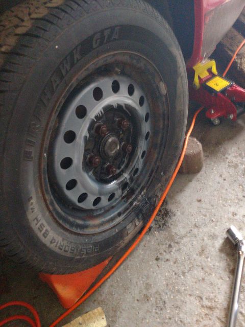 1989 Ford Probe - A close-up view of a car tire and wheel assembly, with a red car jack visible in the background. The tire is resting on an orange wheel cho…