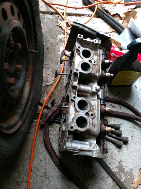 1989 Ford Probe - A disassembled engine cylinder head rests on a concrete surface next to a car tire and an orange extension cord. Several spark plug wires a…