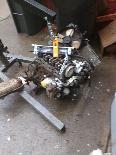 1989 Ford Probe - A disassembled engine is supported by an engine stand and hoist, with a fan and radiator visible. The engine appears to be in a state of re…