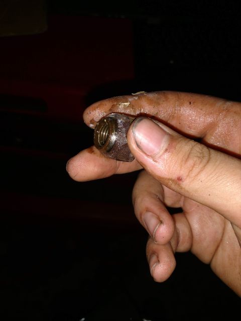 1989 Ford Probe - A dirty hand holds a small, threaded metal part, possibly a nut or bolt, with visible threads and a dark, metallic sheen.