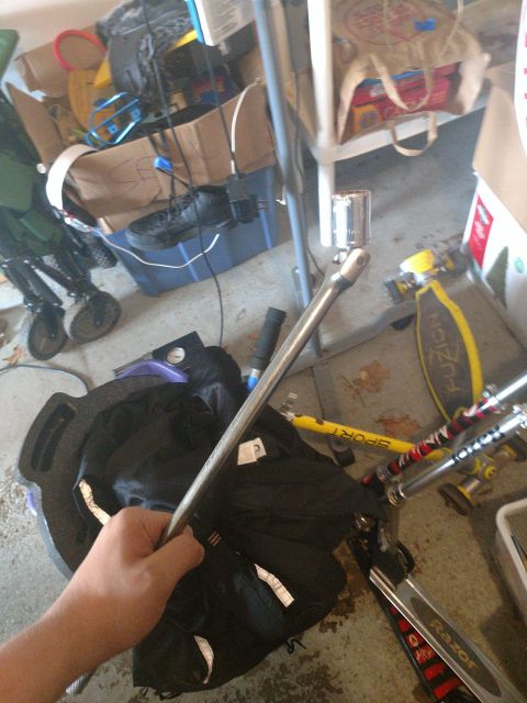 1989 Ford Probe - A hand holds a metal bar with a socket attached, in front of a black bag and various items on a floor.