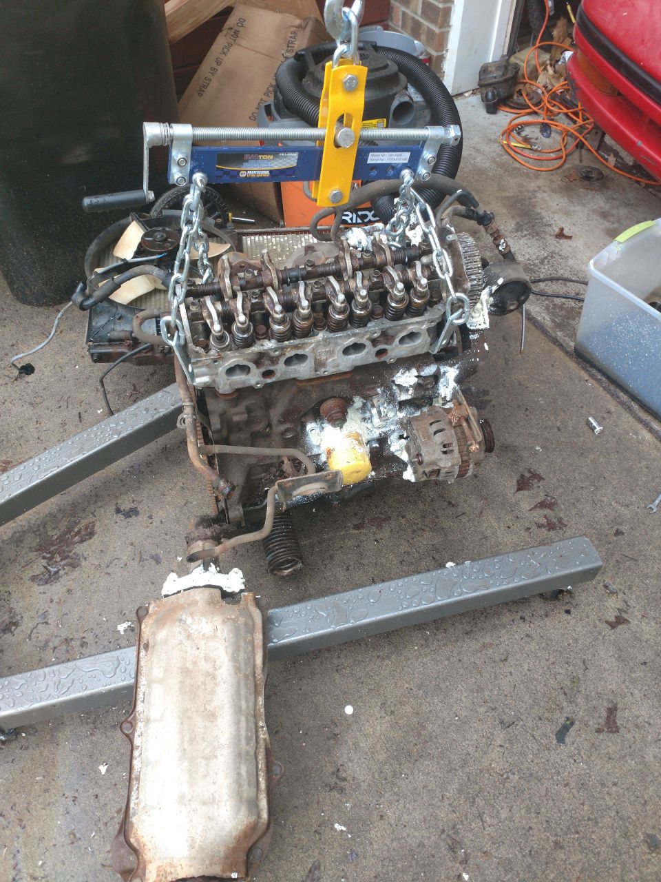 Disassembled engine with catalytic converter on stands, suspended by engine hoist.