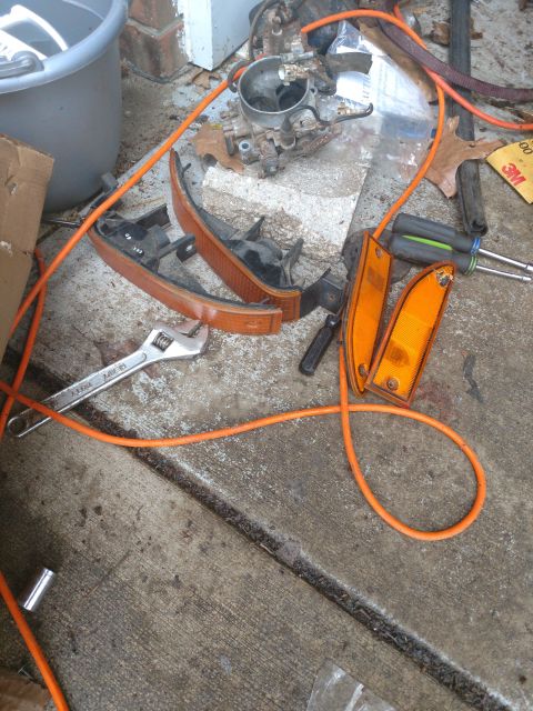 1989 Ford Probe - Several car parts, including orange turn signal lenses, a carburetor, and a wrench, are laid out on a concrete surface next to an orange co…